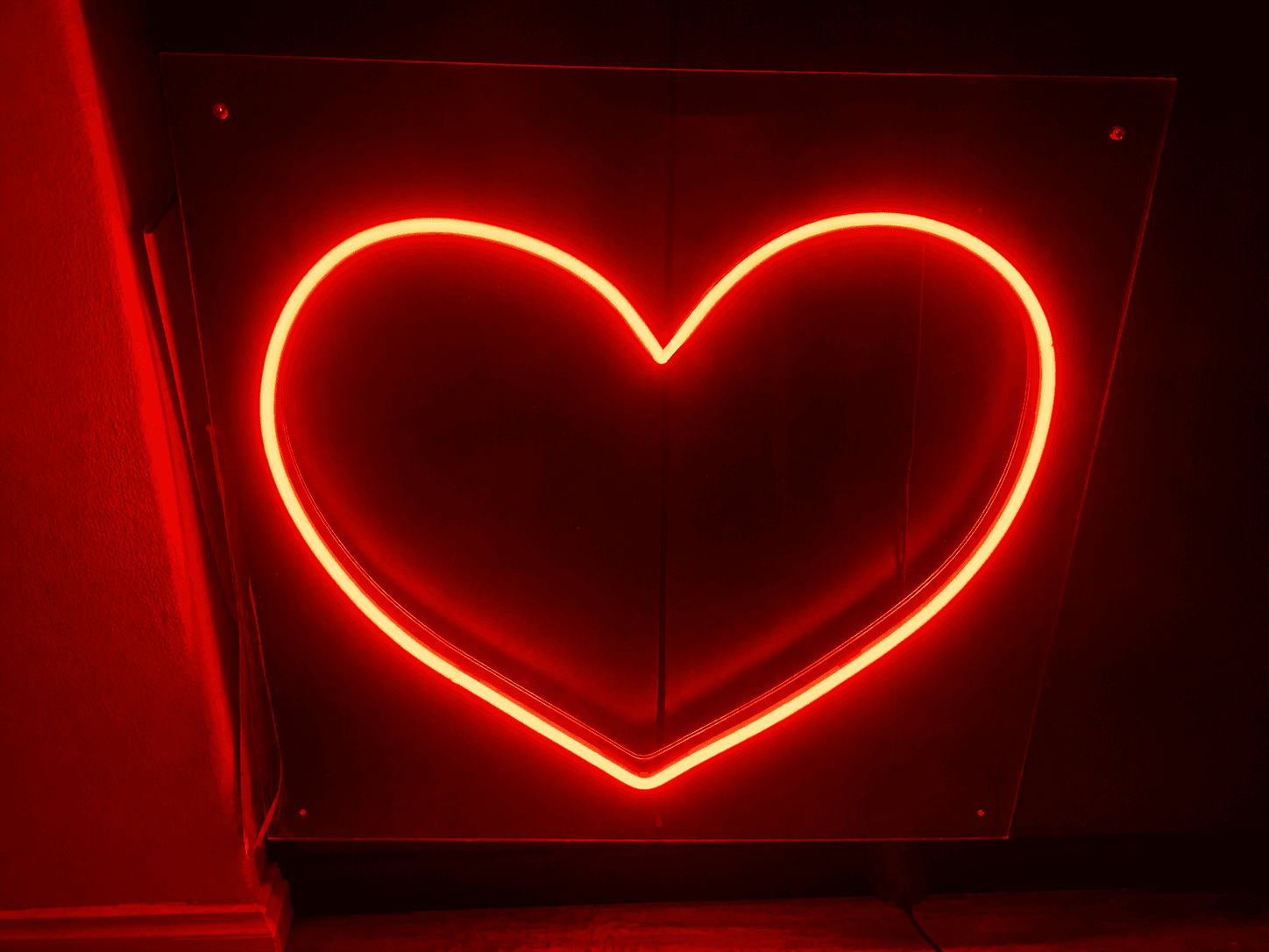 Red neon heart outline glowing against a dark wall