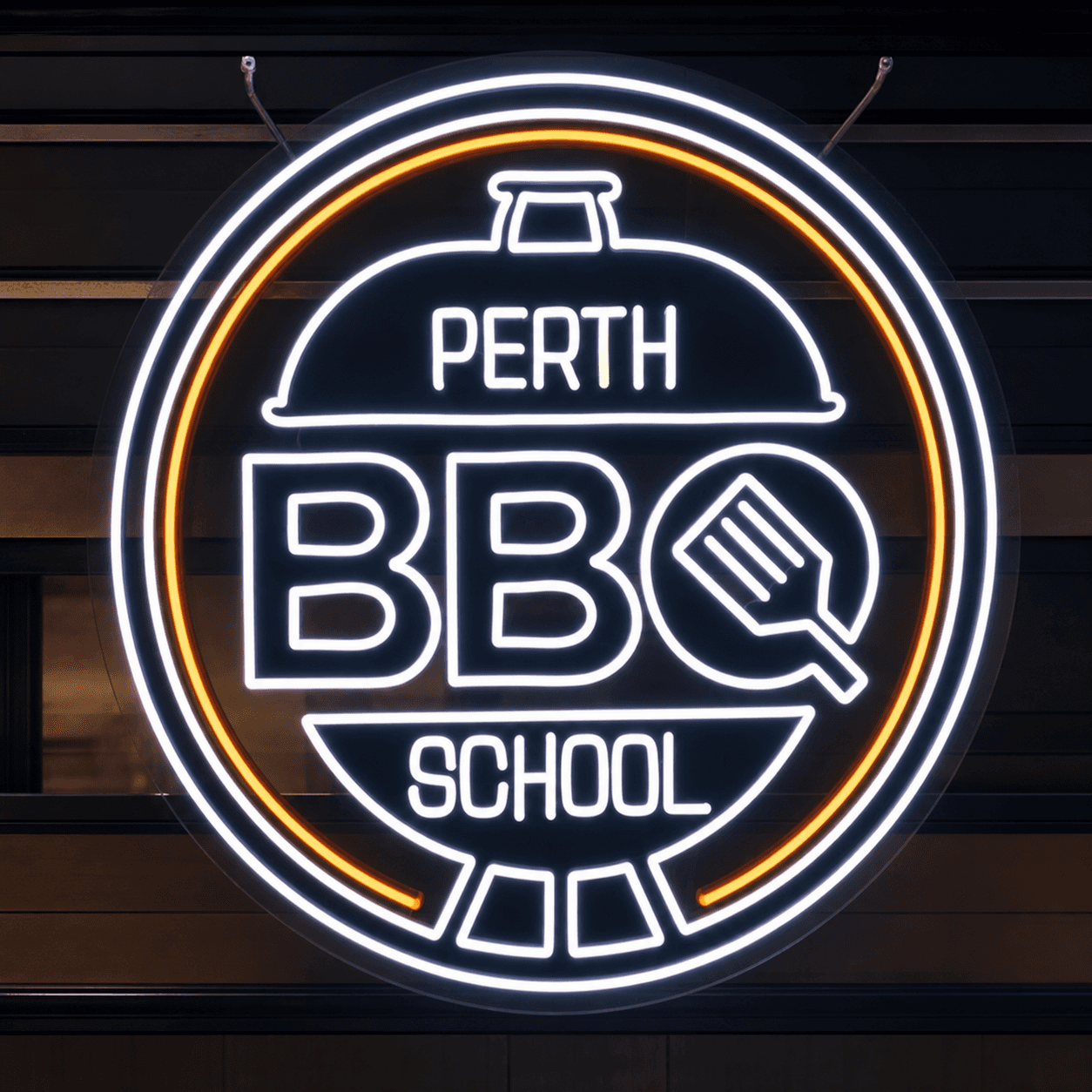 White and amber Perth BBQ School LED neon sign shaped like a BBQ kettle, installed in a shopfront