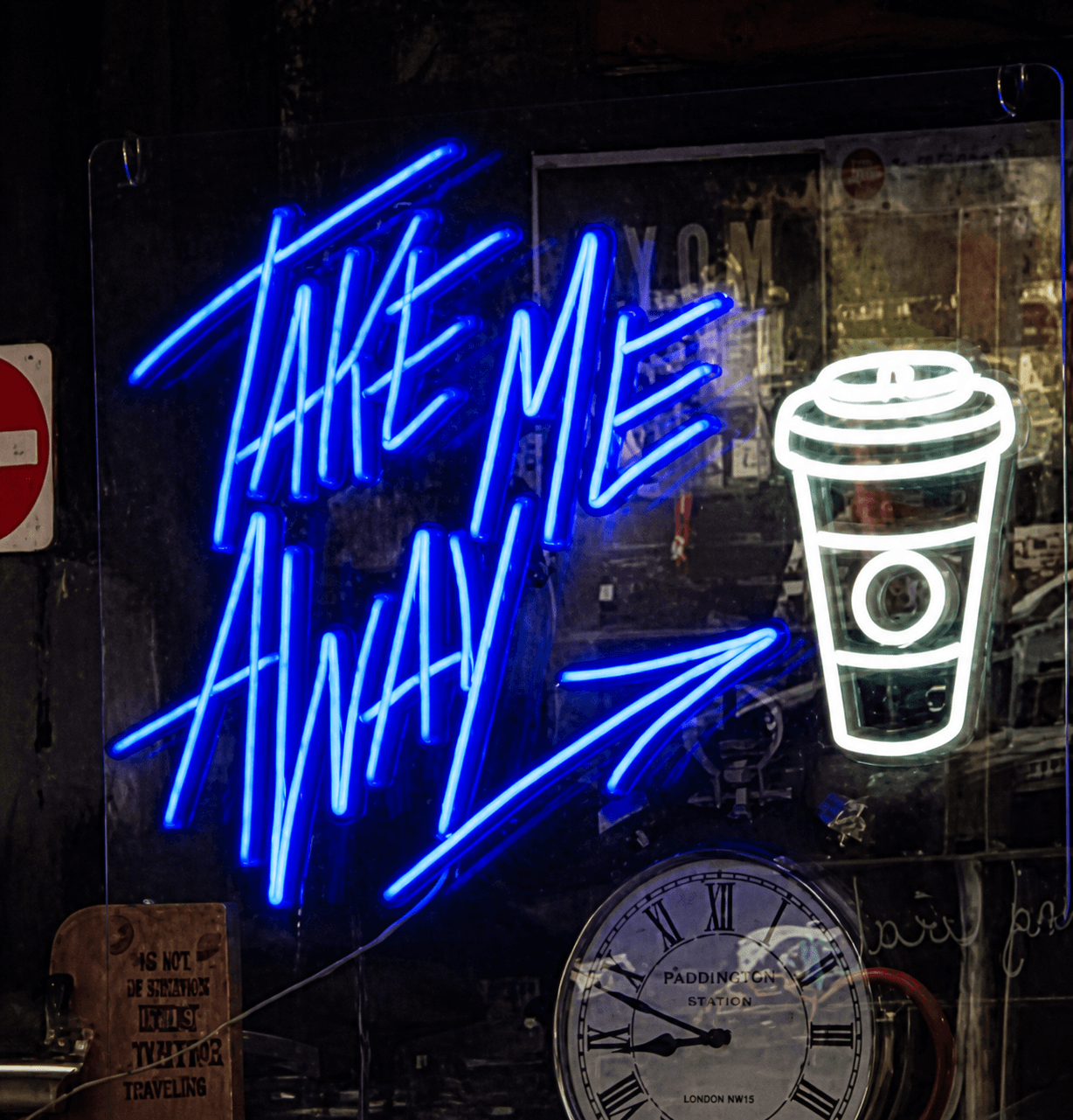 Blue neon sign reading Take Me Away with a white takeaway coffee cup, in a cafe window